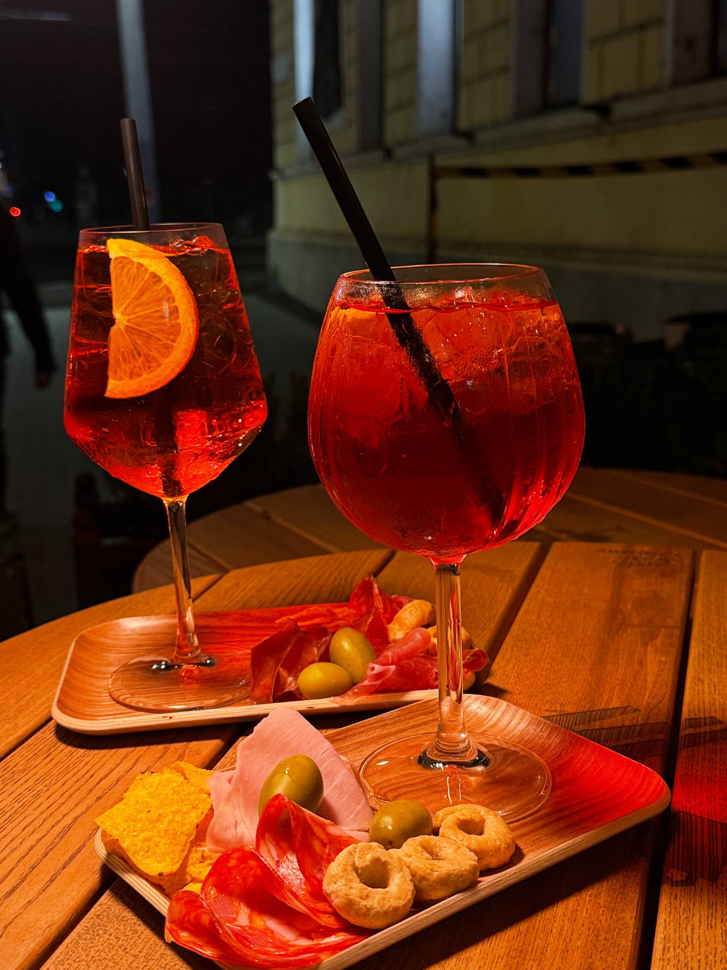 Two spritz cocktails with salumi, olives and taralli on a wooden terrace table at night